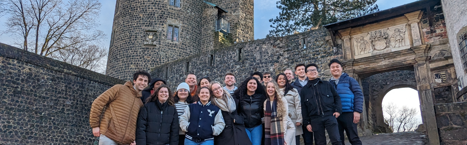 A group of students are gathered outside of a castle. They are posed for a photo and smiling at the camera.